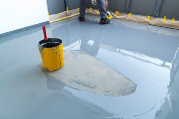 A construction worker renovates balcony floor and spreads watertight resin and glue before chipping and sealing