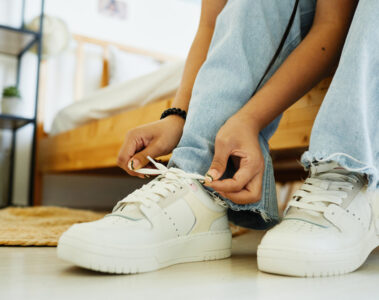 Close up of teenage girl tying shoe laces while sitting on bed ready to go out, copy space