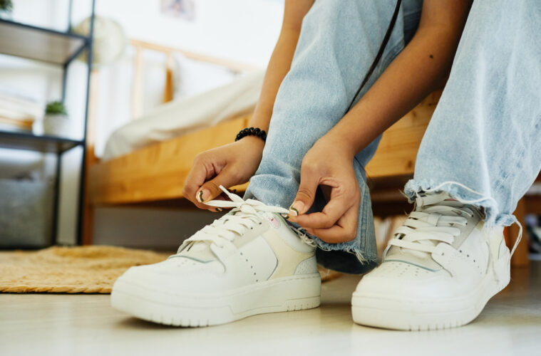 Close up of teenage girl tying shoe laces while sitting on bed ready to go out, copy space